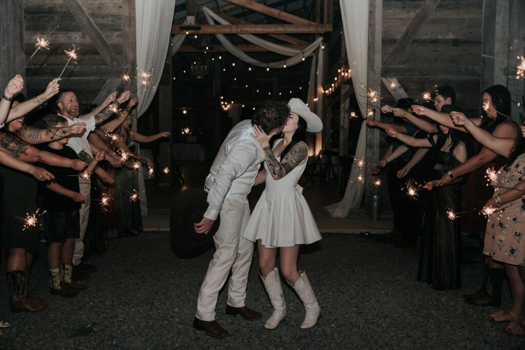 Bride and groom sharing a kiss during a sparkler exit at a rustic barn venue, a classic example of timeless wedding send-off ideas.