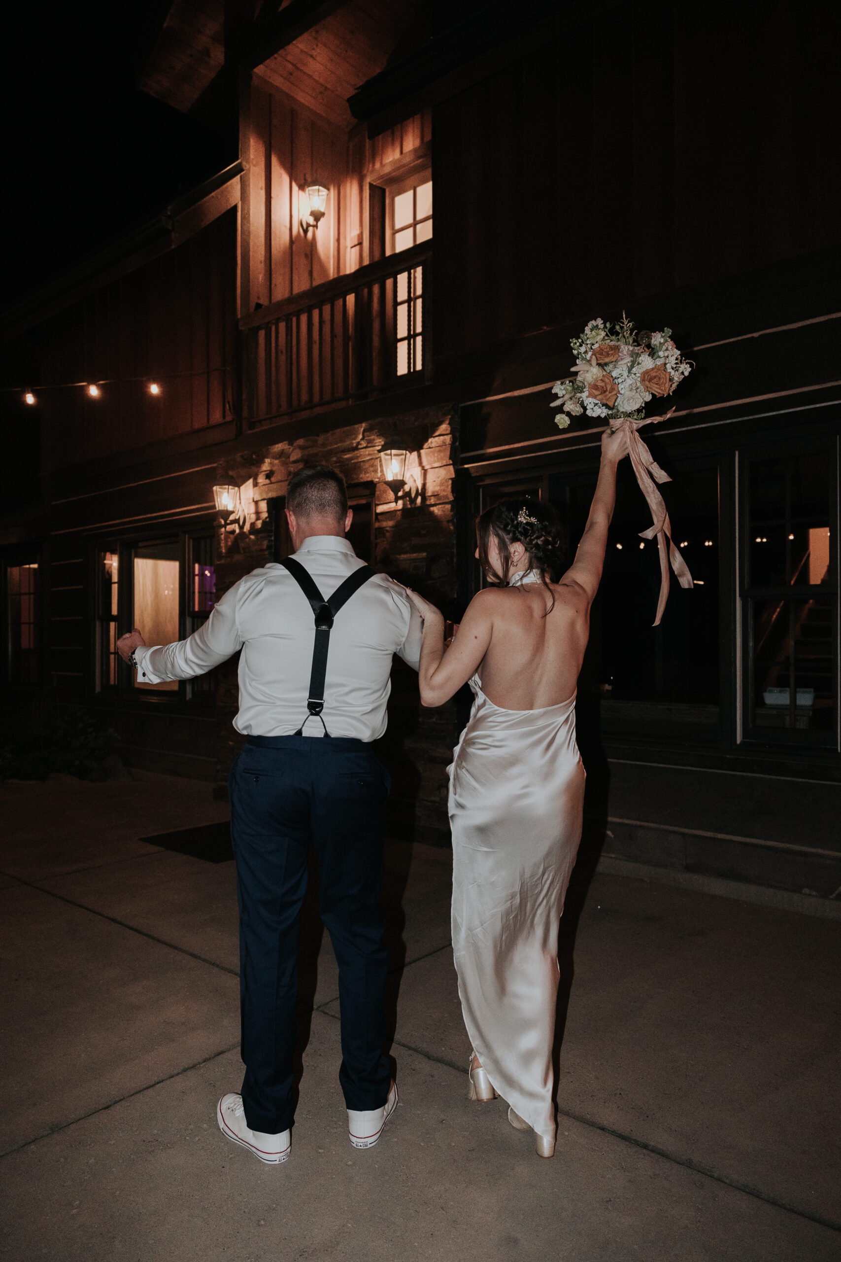 Bride and groom walking away during their nighttime wedding exit, bouquet raised in celebration, showcasing simple and elegant wedding send-off ideas.