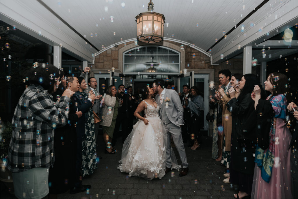 Couple sharing a kiss during a bubble exit surrounded by cheering guests, a beautiful example of wedding send-off ideas captured by a Phoenix wedding photographer.