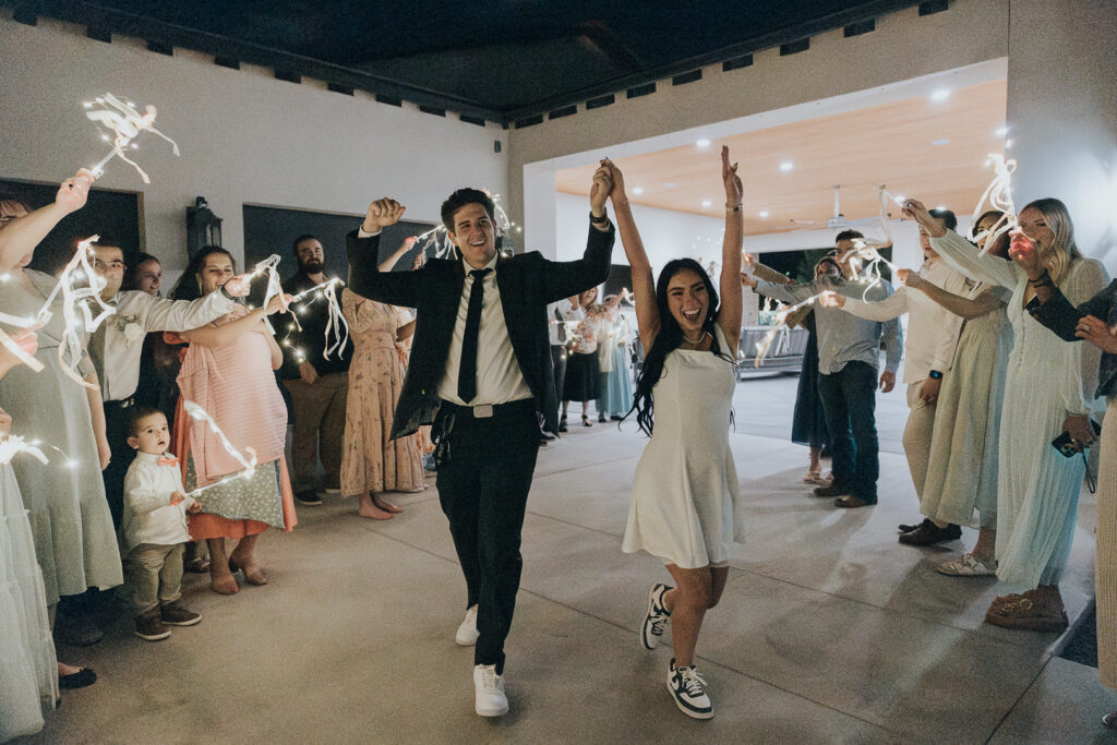 Couple running through a joyful ribbon wand exit surrounded by cheering guests, a fun and creative example of wedding send-off ideas for modern weddings.