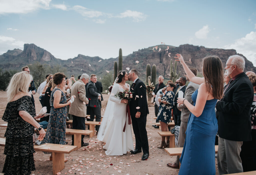 Couple kissing during a petal toss recessional in the Arizona desert, highlighting romantic wedding send-off ideas for outdoor ceremonies.